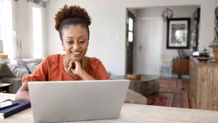 Positive focused young African American freelance professional woman working at laptop at home...