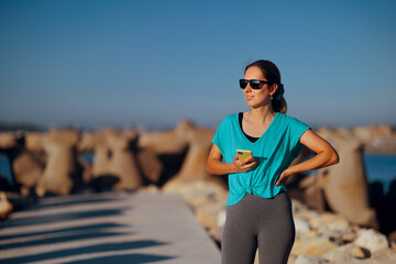 Woman by the Seaside Wearing Sunglasses Checking Mobile Phone. Happy lady reading her messages while taking a walk by the sea