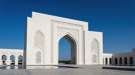 Grand white modern Islamic-style architectural gateway with a large arch and reflective pool under a clear blue sky, showcasing intricate patterns.