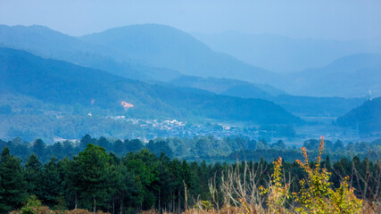 Mountain valley village with forest and misty blue hills in the