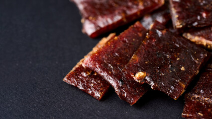 closeup pile of jerky pork on black background with copy space