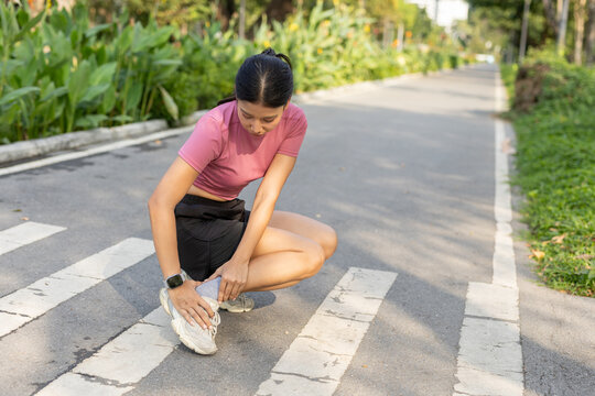 women crouching and holding her ankle in pain on outdoor running track. Sports injury, ankle sprain, workout accident concept. Health care, recovery in active lifestyle.