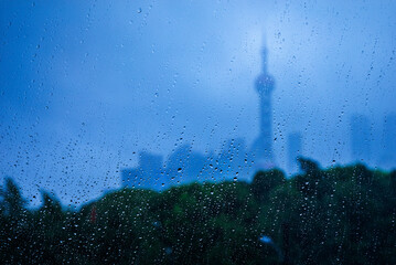 Rain drops on window with blurry city skyline and tower in blue