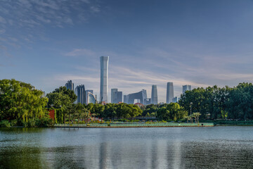 Obraz premium Modern Beijing CBD skyline with skyscrapers reflected on lake in Chaoyang Park, urban nature and business district under clear blue sky.