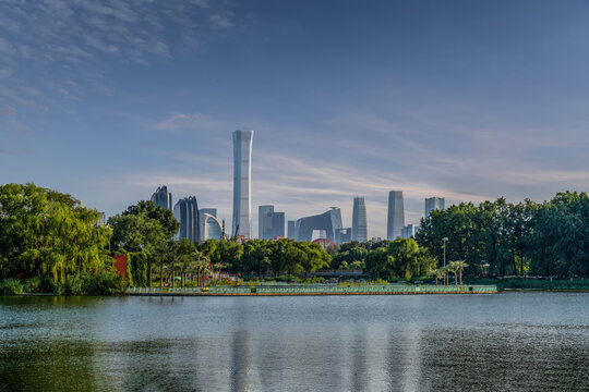 Modern Beijing CBD skyline with skyscrapers reflected on lake in Chaoyang Park, urban nature and business district under clear blue sky.