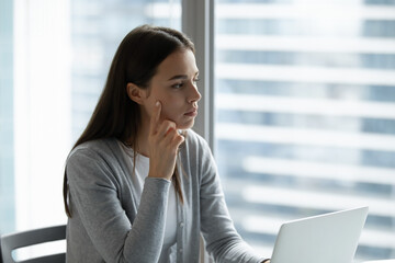 Problem analysis. Serious thoughtful young woman employee manager sit alone at modern office workplace look away from notebook screen visualize innovative project solutions planning marketing campaign