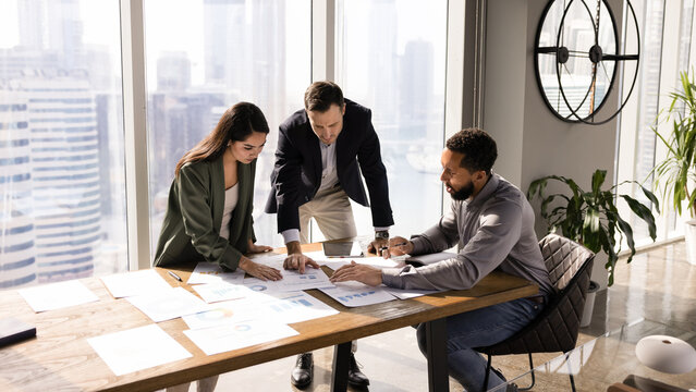 African American manager presenting project to investors, showing paper sales reports on meeting table, explaining marketing research results, discussing business plan. Banner shot