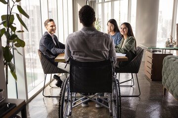 Back view of African American business leader with disability holding meeting with diverse team in office space, sitting in wheelchair, speaking ro positive colleagues at conference table