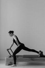 Pilates Reformer machine. Black and white photograph of a slim female executing controlled...