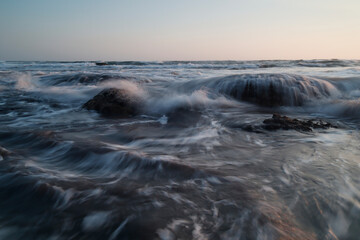 Ocean Water Cascades Over Rocks at a Beach During a Hazy Twilight