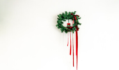 A minimalist Christmas wreath hangs on a clean white wall, with plenty of negative space, emphasizing seasonal warmth.