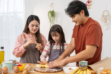 Happy Asian family baking in kitchen with smiling father kneading dough with wife and daughter having fun together