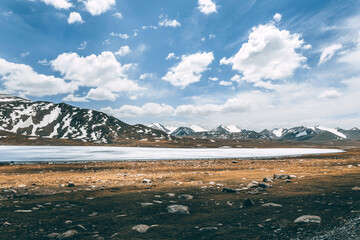 Frozen lake nestled among snow-capped mountains under a bright blue sky with white clouds. Scenic and tranquil winter landscape for travel concept.
