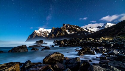 Dramatic Rocky Coastline with Snow-Capped Mountains and Crashing Waves Under a Blue Sky.