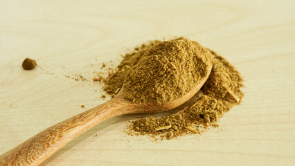 Powdered aquatic animal feed ingredient placed on a wooden spoon over a light natural wood background, representing raw materials used in fish and shrimp feed production