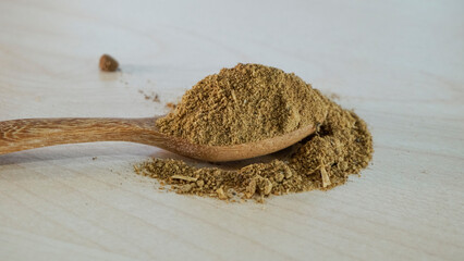 Powdered aquatic animal feed ingredient placed on a wooden spoon over a light natural wood background, representing raw materials used in fish and shrimp feed production