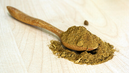 Powdered aquatic animal feed ingredient placed on a wooden spoon over a light natural wood background, representing raw materials used in fish and shrimp feed production