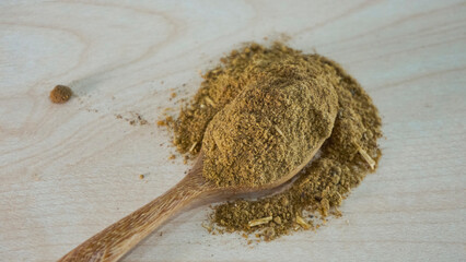 Powdered aquatic animal feed ingredient placed on a wooden spoon over a light natural wood background, representing raw materials used in fish and shrimp feed production