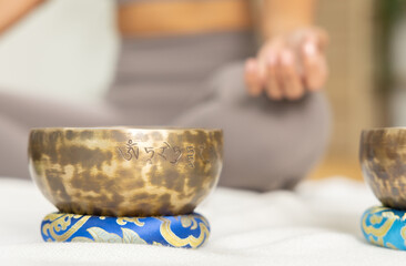 Close up shot of bronze Tibetan singing bowl on cushion with calm mindful woman meditating in lotus...