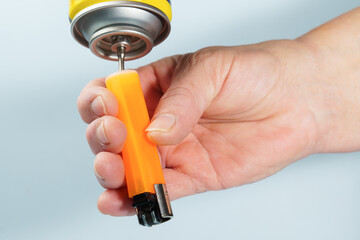Person's hand filling an orange gas lighter with butane fuel from an aerosol can, performing maintenance