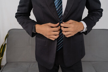 Hands buttoning tailored suit jacket closeup, striped tie and crisp shirt cuffs visible, precise fingers fastening button, focus