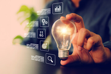 Businessman's hand chooses light bulb or lamp with bright and business icons for human resources or leadership and creativity thinking idea motivation or vision and knowledge learning. © Jintana