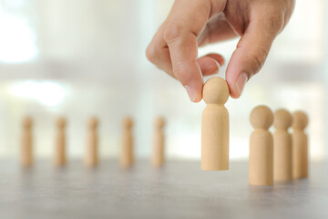 Businessman's hand chooses wooden person stands for HR human resources personal leader training skill or leadership and challenge business team player and organization management teamwork.