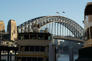 Fototapeta premium Iconic Sydney Harbour Bridge and Massive Pylon Towers Framed by a Classic Ferry Under a Clear Blue Morning Sky