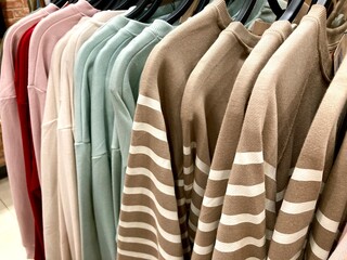 assorted colorful sweaters and striped sweatshirts hanging on a retail clothing rack