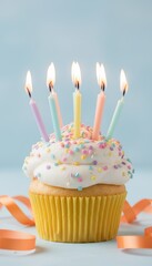 birthday cupcake with lit candles and sprinkles on blue background with orange ribbon streamers, festive party dessert, celebration concept with copy space