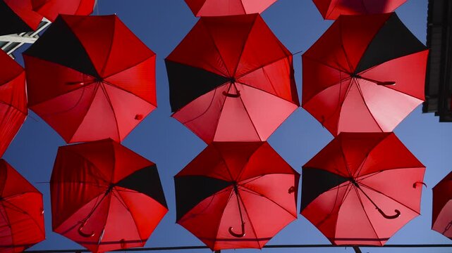 Red umbrellas hang over pedestrian city street against blue sky. Vbrant outdoor decoration for festive and festival occasion. Umbrella installation provides sun protection during hot season.
