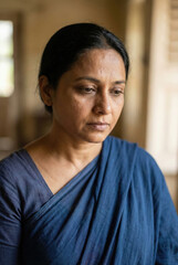 Obraz premium Sad or depressed middle-aged Indian woman looking down indoors, symbolizing mental health, loneliness, and emotional struggle.