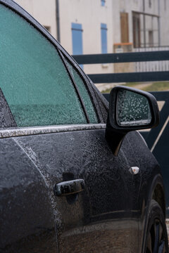 Frost covered black car with icy windows and mirror in winter morning