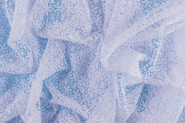 Background image of chaotic waves of openwork white fabric with floral ornaments. Abstract background of white guipure. delicate texture of folds.