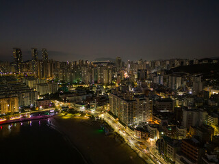 Obraz premium Aerial drone view of Busan city skyline at night with illuminated buildings and coastal waterfront, South Korea