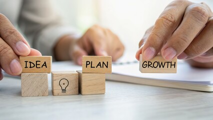 Hands arranging wooden blocks labeled with "IDEA," "PLAN," and "GROWTH" on a table, symbolizing business strategy and development.