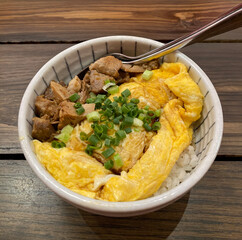 Rice bowl topped with braised pork and soft scrambled egg, garnished with fresh chopped green onions, served in a ceramic bowl on a wooden table. This image represents Asia's homemade rice