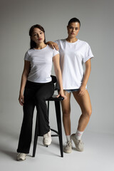 Female Models Pose In Relaxed Settings Wearing White Shirts With Focused Lighting Highlighting Fabric Details