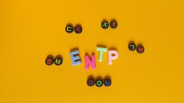 Toy alphabet blocks spelling ENTP, an MBTI personality type, surrounded by Korean characters symbolizing challenge, flexibility, out-of-the-box thinking, and wit on a bright yellow background.