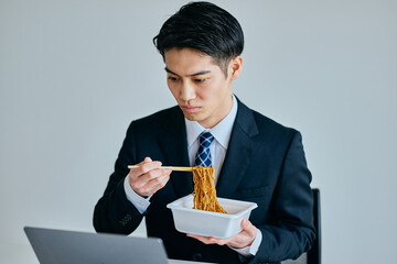 カップ焼きそばを食べながら仕事をする20代の若い男性
