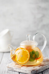 Glass teapot with hot citrus tea from oranges, lemons, apples and mint. Healthy drink on white wooden background