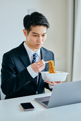 カップ焼きそばを食べながら仕事をする20代の若い男性