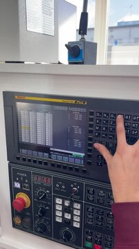 CNC machine operator enters program data into the machine's computer using the control panel keyboard, setting up parameters for precise workpiece machining.