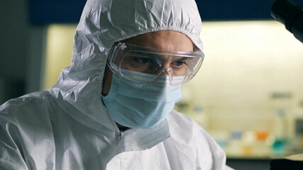 Scientist in protective gear, focused expression, soft light, blurred lab background; dedication to scientific discovery in action.