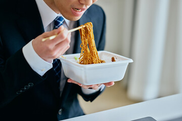 カップ焼きそばを食べながら仕事をする20代の若い男性