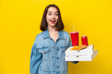 Young Ukrainian woman holding fast food isolated on yellow background with surprise facial...