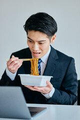 カップ焼きそばを食べながら仕事をする20代の若い男性