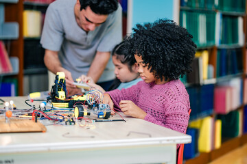 Instructor teaches robotics concepts by demonstrating electronic assembly, support student understands, STEM education foundation, collaborative learning process inside library classroom.