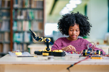 African American girl practices STEM education by building robotic arm, exploring electronics, coding basics, engineering mindset inside school library..