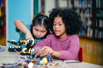 Young students collaborate on robotics project using electronic components and robotic arm kit inside library. Concept teamwork, STEM education, diversity, creativity, and future technology learning.
